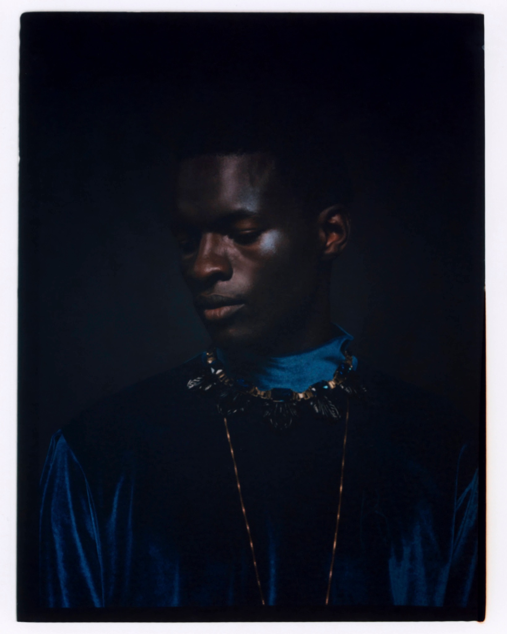 Low-key portrait of a model in a blue shirt and dark outerwear, looking to the side.