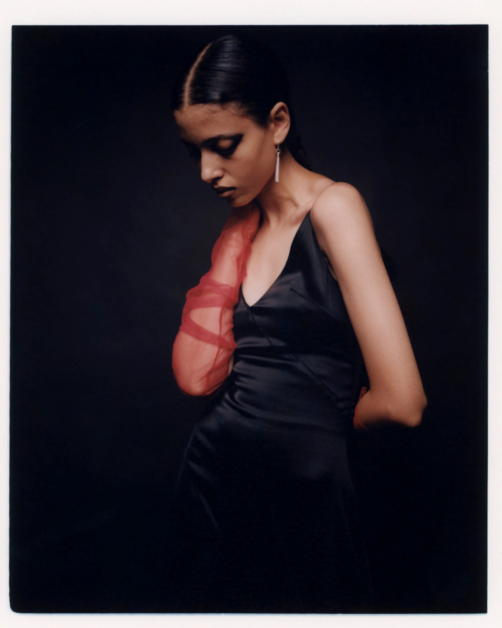 Model looking down in a black dress, with a red translucent detail across the chest.