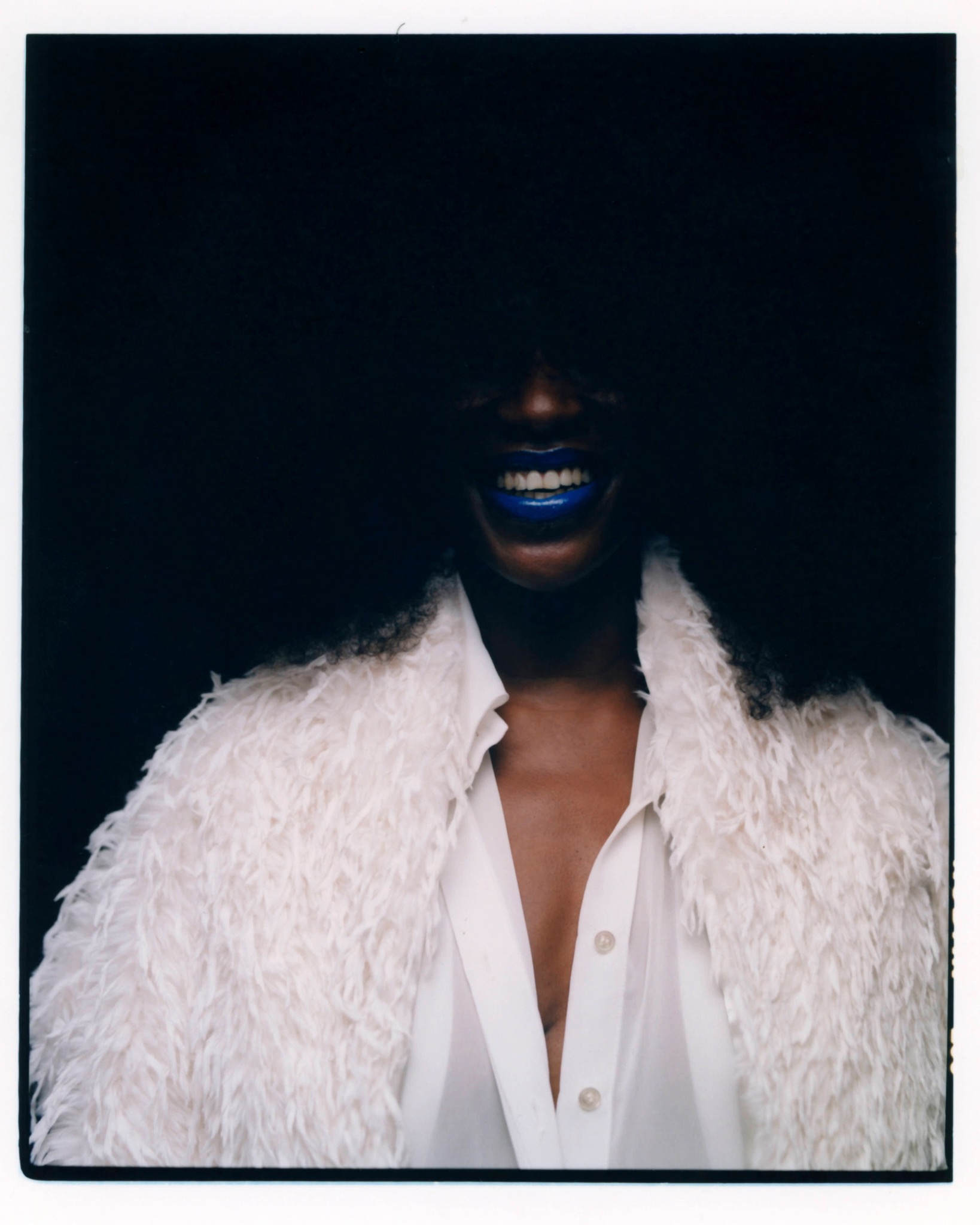 Close-up of a smiling model wearing a white textured coat over an open shirt against a dark background.