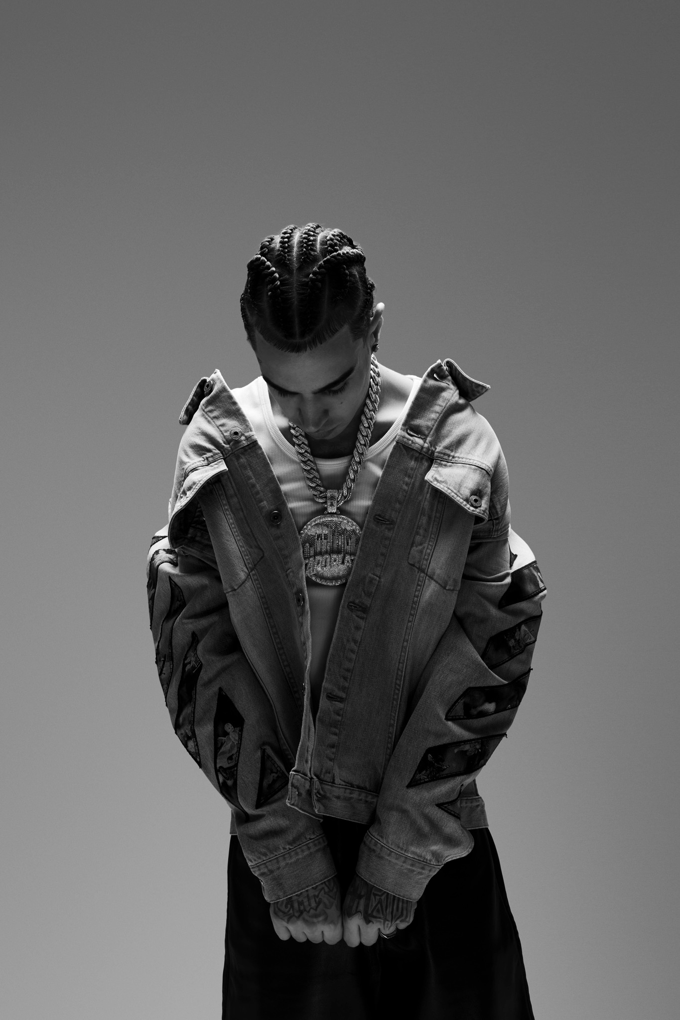 Black-and-white portrait of Capo Plaza looking down in an oversized jacket, his hands held together.