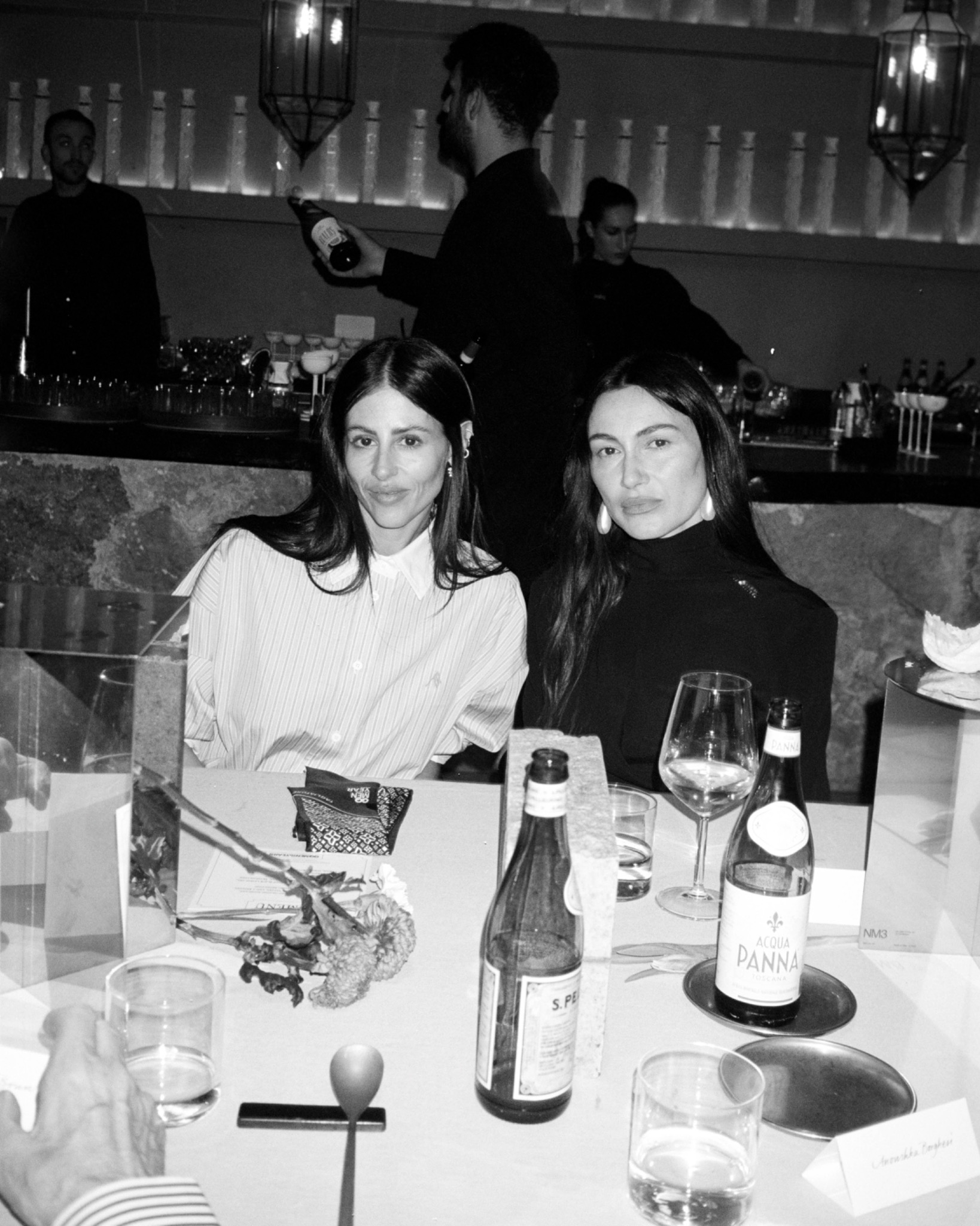 Black-and-white portrait of Gilda and Giorgia seated together at a restaurant table with glasses and bottles.