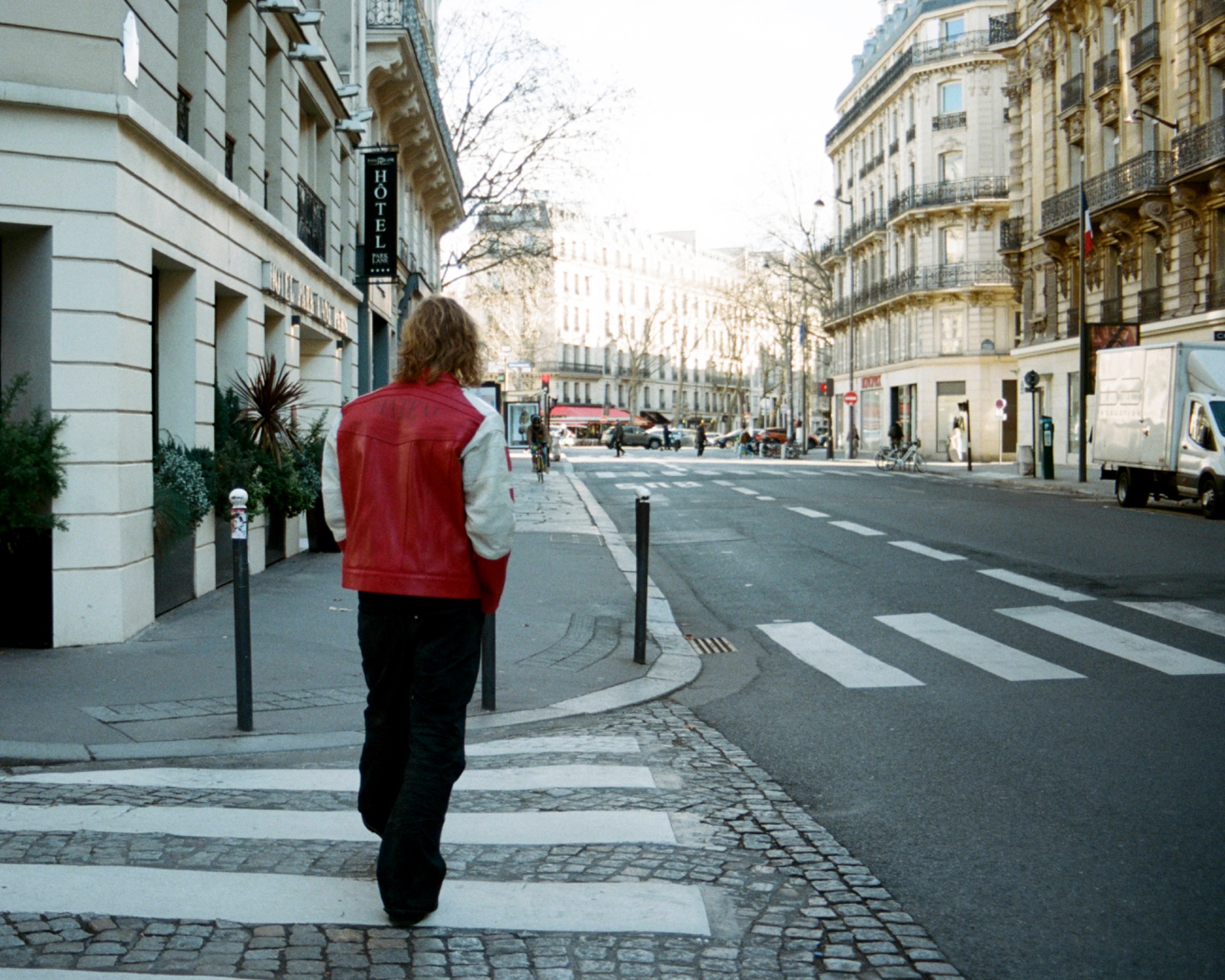 Jacopo seen from behind walking along a city street in a red vest, light shirt and dark trousers.