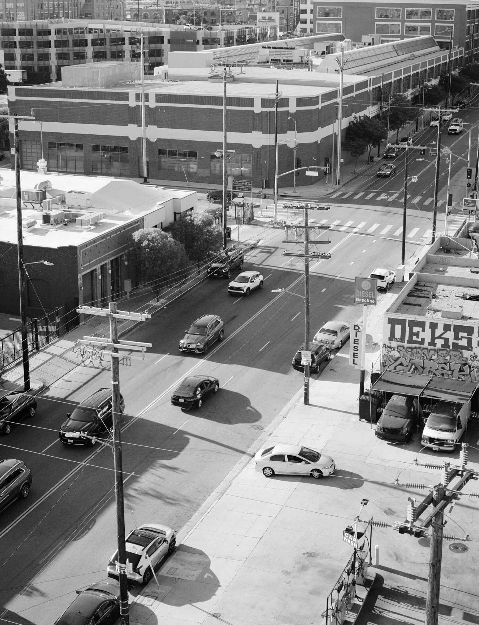 Black-and-white view from above of a downtown Los Angeles intersection, with cars, buildings and overhead wires.