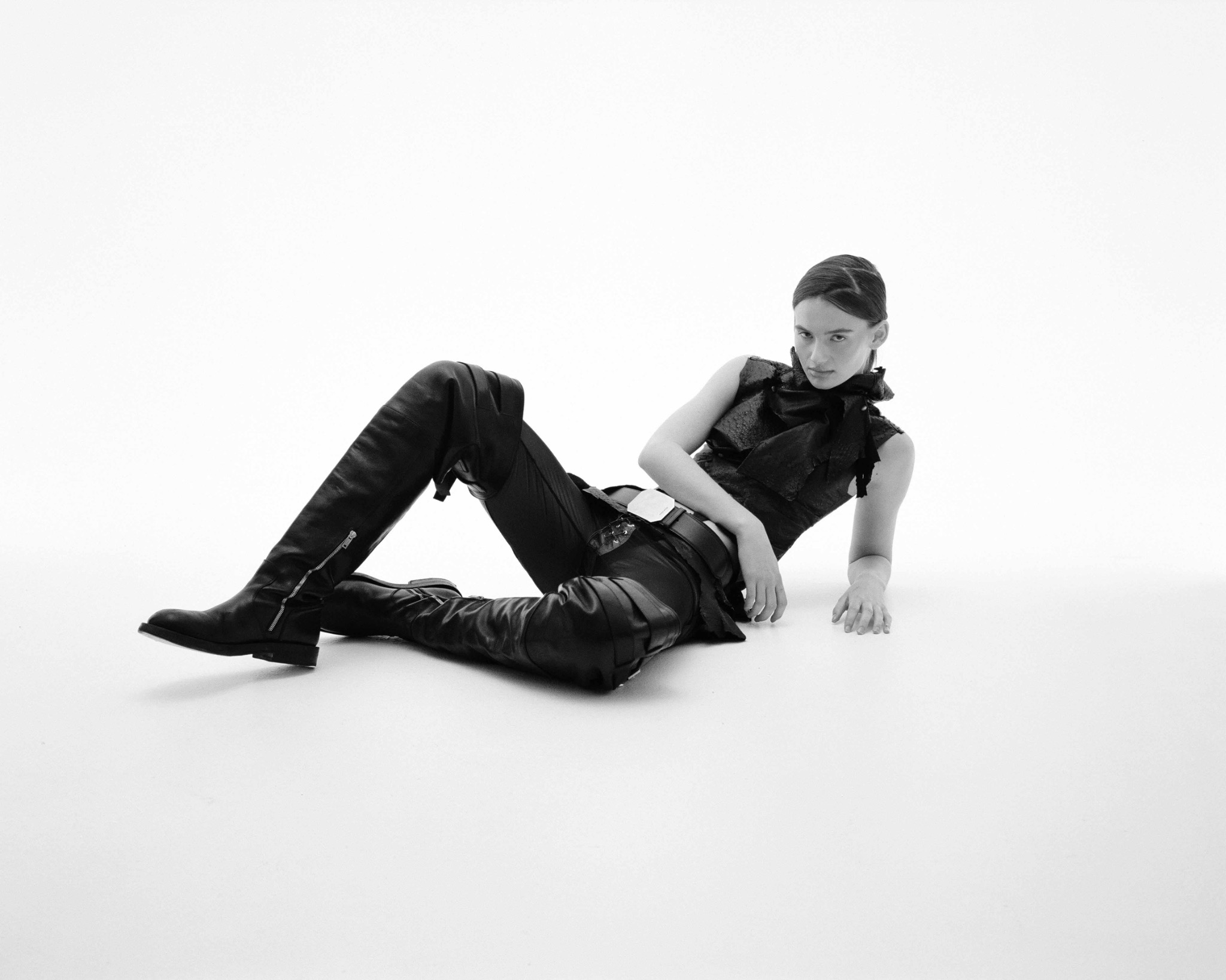 Black-and-white studio portrait of Savea reclining on the floor in a dark sleeveless top, trousers and boots.